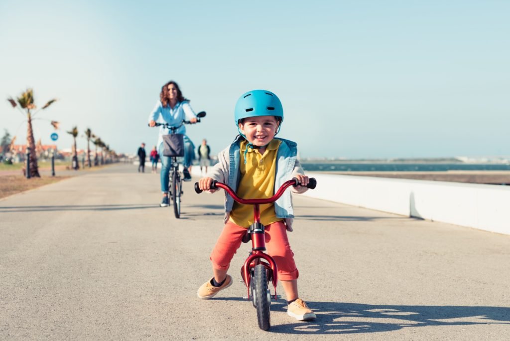 Little kid riding a balance bike with his mother on a bicycle