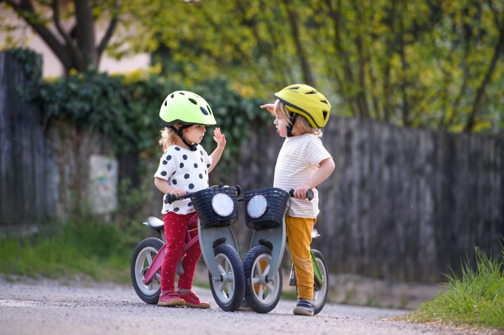 Small children boy and girl with helmets and balance bikes outdoors playing