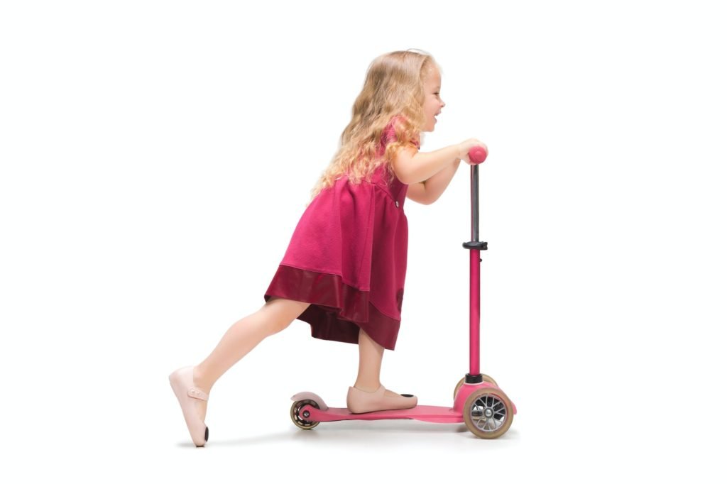 Smiling cute toddler girl three years riding a scooter over white background