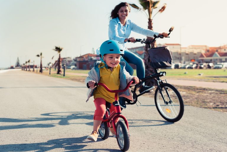 Little kid riding a balance bike with his mother on a bicycle
