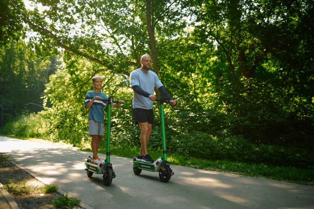 Father and boy riding on kick scooters in park